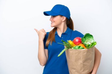 Genç teslimatçı kadın, beyaz arka planda izole edilmiş bir paket yiyecek alıyor. Yan tarafı göstererek ürünü sunuyor.