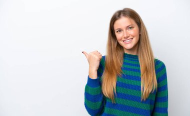 Beyaz arka planda izole edilmiş genç beyaz kadın bir ürünü sunmak için kenarı işaret ediyor.