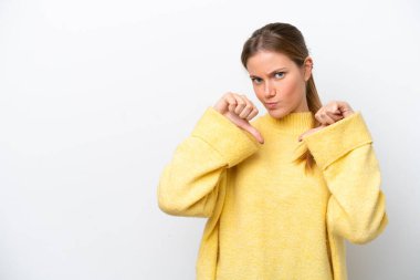 Beyaz arka planda izole edilmiş genç beyaz kadın baş parmağını iki eliyle aşağı gösteriyor.