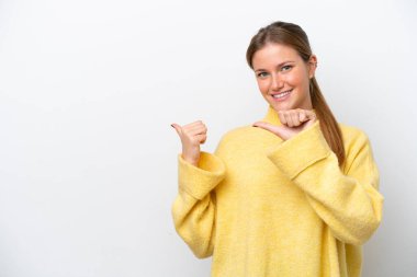 Beyaz arka planda izole edilmiş genç beyaz kadın bir ürünü sunmak için kenarı işaret ediyor.