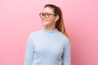 Pembe arka planda soyutlanmış genç beyaz kadın yana bakıyor ve gülümsüyor.