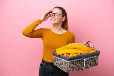Pembe arka planda izole edilmiş çamaşır sepetini tutan beyaz bir kadın.