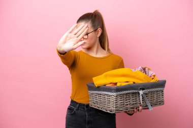 Pembe arka planda izole edilmiş çamaşır sepetini tutan beyaz bir kadın dur hareketi yapıyor ve hayal kırıklığına uğruyor.