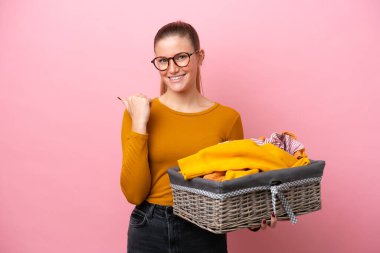 Genç beyaz kadın pembe arka planda izole edilmiş bir çamaşır sepeti tutuyor. Yan tarafı göstererek bir ürün sunuyor.
