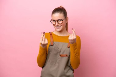 Önlüklü kadın pembe arka planda izole edilmiş para hareketi yapıyor.