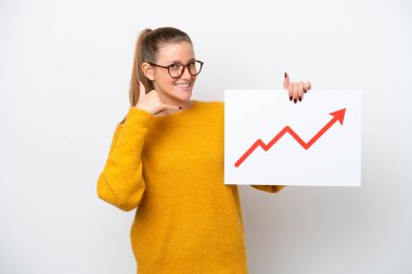 Beyaz arka planda izole edilmiş genç beyaz bir kadın elinde büyüyen bir istatistik okuyla bir tabela tutuyor ve telefon jesti yapıyor.