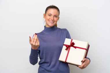Beyaz arka planda izole edilmiş beyaz bir hediye tutan genç beyaz bir kadın bizimle gelmesi için davet ediyor. Gelmene sevindim.