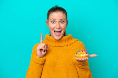 Mavi arka planda izole edilmiş turta tutan beyaz bir kadın harika bir fikre işaret ediyor.