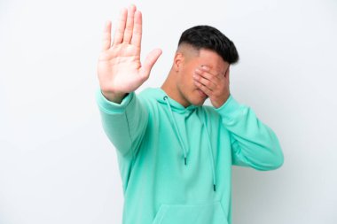 Beyaz arka planda izole edilmiş beyaz tenli yakışıklı genç adam jesti durduruyor ve yüzünü kapatıyor.