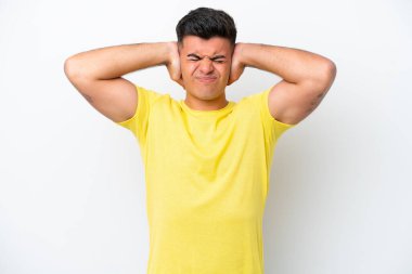 Beyaz arka planda izole edilmiş beyaz, yakışıklı genç adam hayal kırıklığına uğramış ve kulaklarını kapatmış.