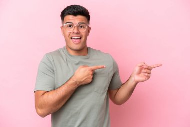 Young caucasian handsome man isolated on pink background surprised and pointing side