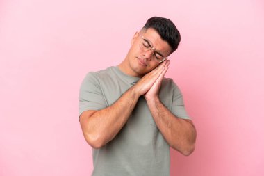 Pembe arka planda izole edilmiş beyaz, yakışıklı genç bir adam uyku jesti yapıyor.