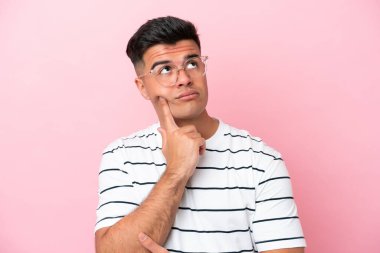 Pembe arka planda gözlüklü ve yukarı bakan beyaz tenli yakışıklı bir adam.