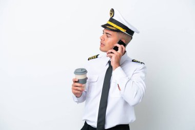 Uçak pilotu beyaz arka planda izole edilmiş beyaz bir beyaz adam kahve alıp götürmek için elinde bir cep telefonu var.