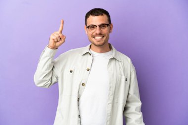 İzole edilmiş mor arka planı olan Brezilyalı bir adam harika bir fikre işaret ediyor.