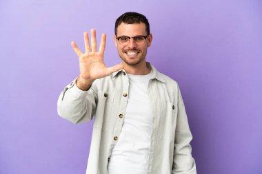 İzole edilmiş mor arka plan üzerinde Brezilyalı adam parmaklarıyla beşi sayıyor