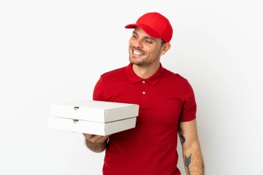 Pizza teslimatçısı üniformalı adam izole edilmiş beyaz duvarın üzerinden pizza kutuları alıp yan tarafa bakıyor ve gülümsüyor.