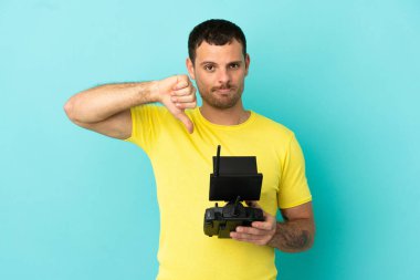 İzole edilmiş mavi arkaplan üzerinde uzaktan kumandayla uzaktan kumanda tutan Brezilyalı bir adam negatif ifadeyle baş parmağını aşağı gösteriyor