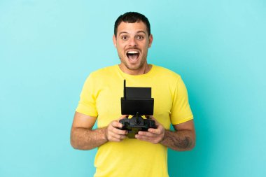 Brezilyalı bir adam uzaktan kumandayla izole edilmiş mavi arkaplan üzerinde sürpriz yüz ifadesiyle