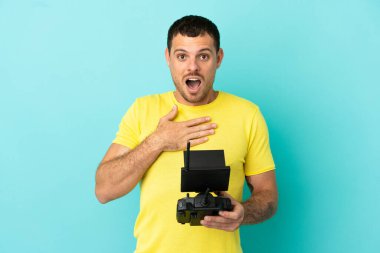 Brezilyalı bir adam mavi arka plan üzerinde uzaktan kumanda tutuyor sağa bakarken şaşırmış ve şok olmuş.