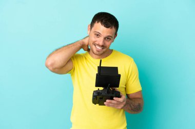 Brazilian man holding a drone remote control over isolated blue background laughing