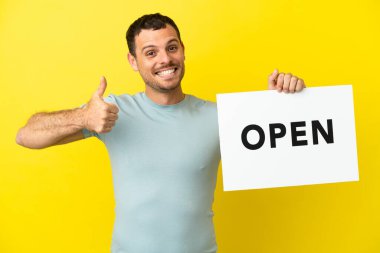 İzole edilmiş mor arka planda Brezilyalı bir adam. Elinde başparmağıyla açık bir pankart tutuyor.