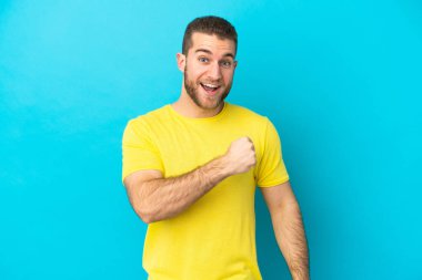 Mavi arka planda izole edilmiş yakışıklı beyaz adam zaferi kutluyor.