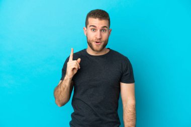 Genç, beyaz, mavi arka planda izole edilmiş genç bir adam çözümü bulmak için parmağını kaldırıyor.