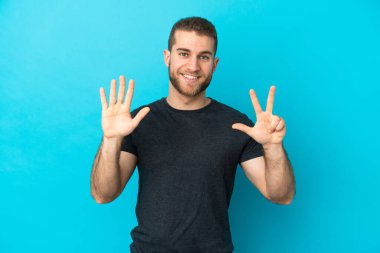 Mavi arka planda izole edilmiş yakışıklı beyaz adam parmaklarıyla sekizi sayıyor.