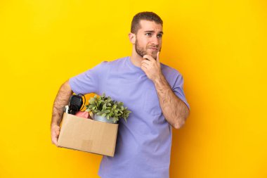 Genç Kafkasyalı, sarı arka planda izole edilmiş eşyalarla dolu bir kutuyu alırken harekete geçiyor.