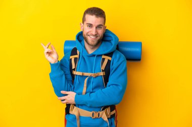 Sarı arka planda izole edilmiş büyük bir sırt çantası olan beyaz bir dağcı.