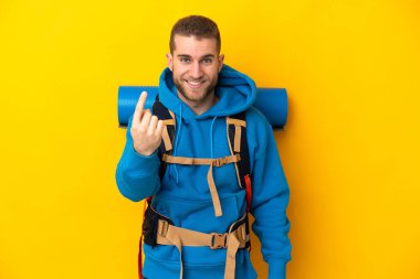 Sarı arka planda izole edilmiş büyük sırt çantalı beyaz bir dağcı geliyor.