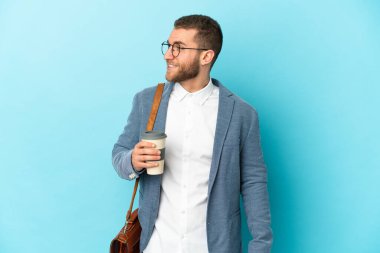 Kafkasyalı genç işadamı mavi arka planda izole edilmiş, yana bakıyor ve gülümsüyor.