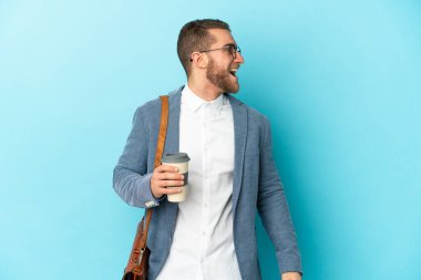 Kafkasyalı genç işadamı mavi arka planda izole edilmiş. Yan pozisyonda gülüyor.