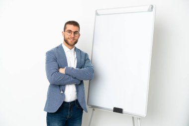 Beyaz arka planda beyaz tenli, beyaz panoda sunum yaparken kolları çapraz olan yakışıklı beyaz bir adam.