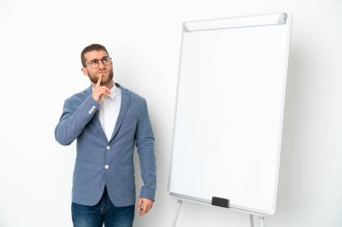 Beyaz arka planda izole edilmiş beyaz panoda sunum yapan genç bir iş kadını yukarı bakarken şüphe duyuyor.