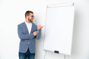 Beyaz arka planda izole edilmiş beyaz panoda sunum yapan genç bir iş kadını bir ürünü sunmak için kenarı işaret ediyor.