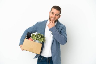 Beyaz arka planda izole edilmiş eşyalarla dolu bir kutuyu alıp yan tarafa bakıp gülümseyen genç bir beyaz.