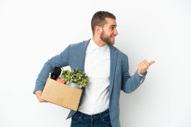 Beyaz arka planda izole edilmiş eşyalarla dolu bir kutuyu kaldırırken harekete geçen beyaz tenli genç, bir ürünü sunmak için kenarı işaret ediyor.