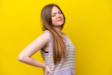 Genç, beyaz bir kadın, sarı arka planda izole edilmiş, çabaladığı için sırt ağrısı çekiyor.