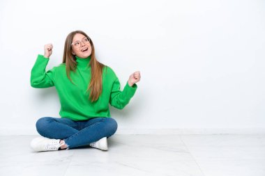 Beyaz arka planda izole bir şekilde yerde oturan beyaz bir kadın zaferi kutluyor.