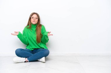 Beyaz arka planda izole bir şekilde yerde oturan genç beyaz kadın ellerini kaldırırken şüpheye düşüyor.