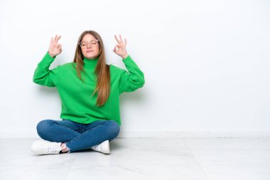 Yerde beyaz arka planda Zen pozunda yalnız oturan beyaz bir kadın.