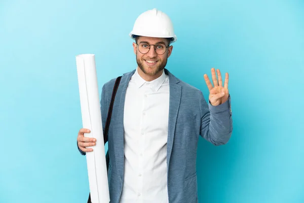 Young architect man with helmet and holding blueprints over isolated background happy and counting four with fingers