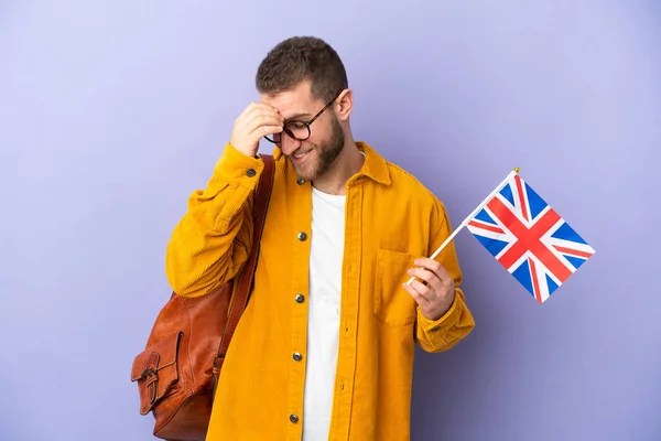 年轻的高加索男子举着一面英国国旗 被紫色背景的笑声隔开 — 图库照片