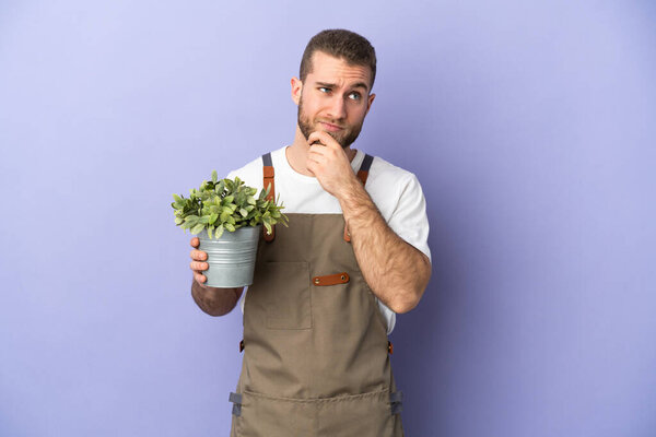 Gardener caucasian man holding a plant isolated on yellow background and looking up