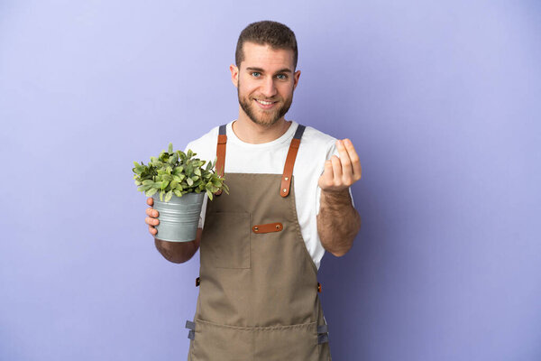 Gardener caucasian man holding a plant isolated on yellow background making money gesture