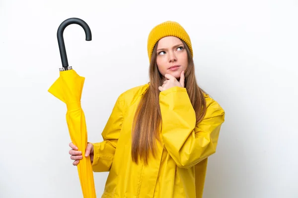 若いですCaucasian女性でレインプルーフコートと傘は疑問を持っている白の背景に隔離 — ストック写真