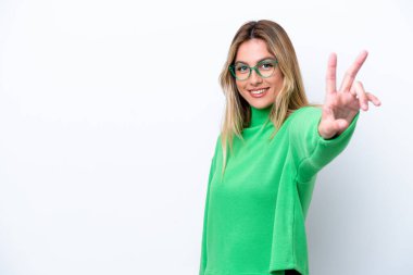 Genç Uruguaylı kadın beyaz arka planda izole edilmiş gülümsüyor ve zafer işareti gösteriyor.