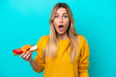 Genç Uruguaylı kadın elinde saşimi tutarken mavi arka planda şaşırmış bir yüz ifadesi var.